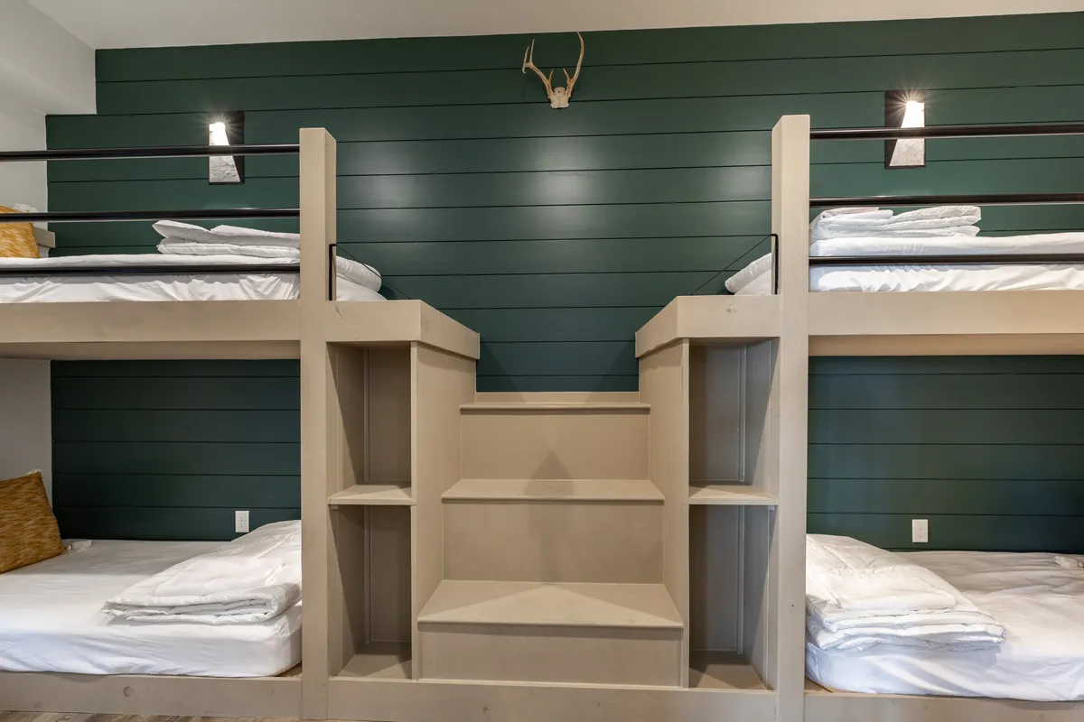 The image features a playful bunk room with built-in bunk beds, a wooden staircase, and antler decor. The design is both comfortable and whimsical, making it a perfect retreat for kids to enjoy sleepovers or quiet moments before bedtime.