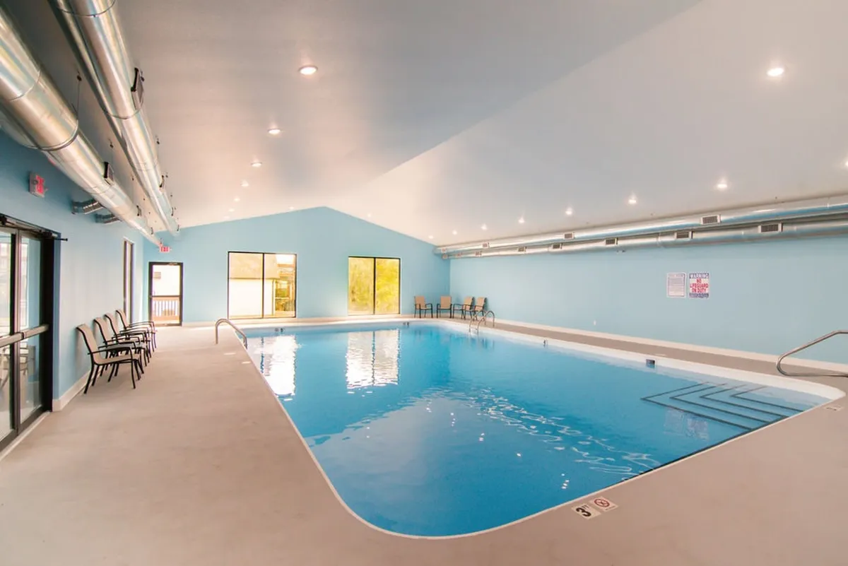 A spacious indoor pool area with large windows, a serene seating zone, and clear blue water. The tranquil mood invites year-round swimming and socializing in a bright, refreshing environment.