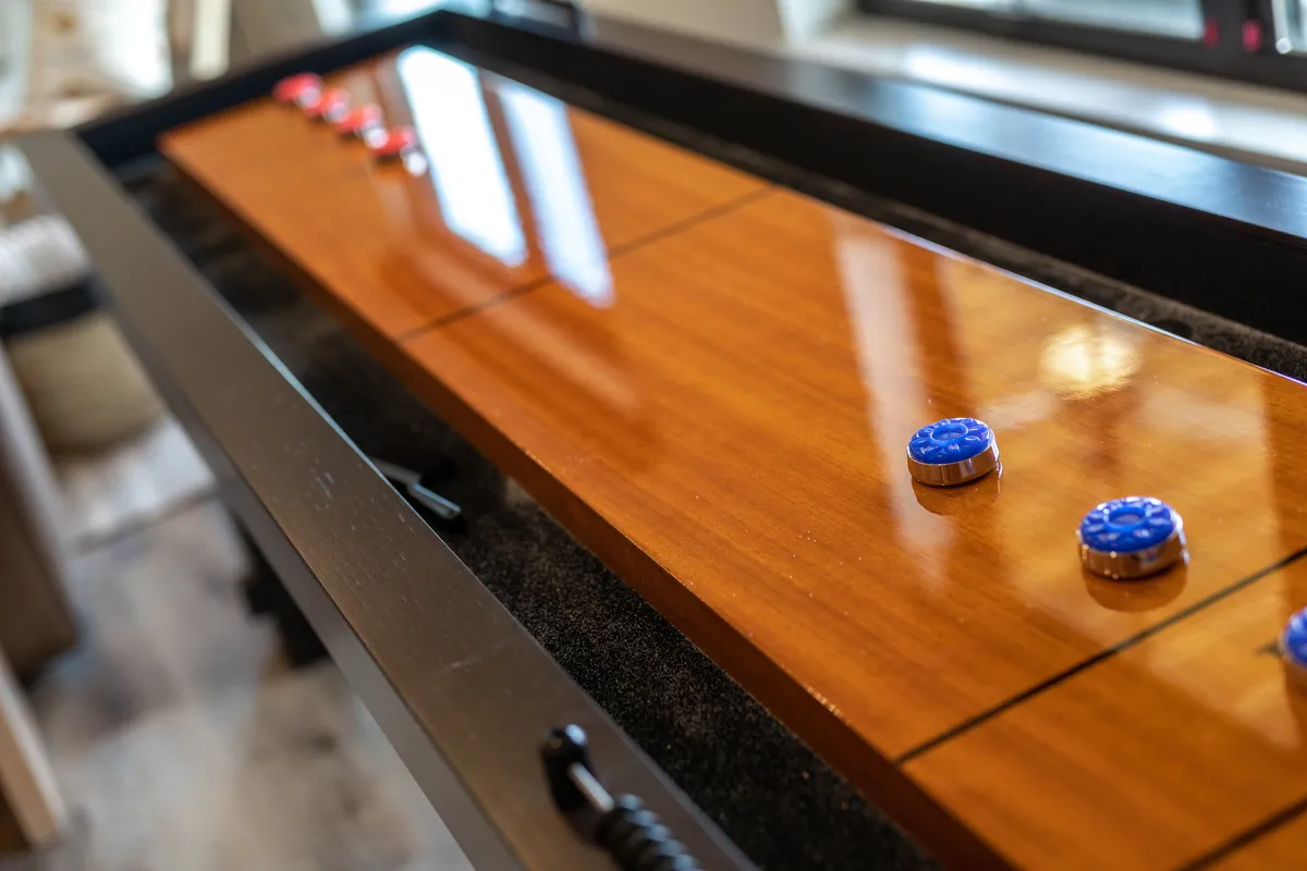 An inviting interior scene focusing on a shuffleboard table with colorful game pieces, set in a lively game room environment designed for friendly competition and group entertainment.