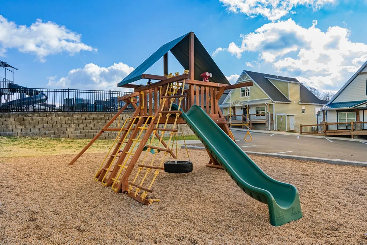 A cheerful playground exterior featuring a slide and swing set, designed for children to play and socialize. The structure stands on a safe surface, surrounded by open space and bright daylight.