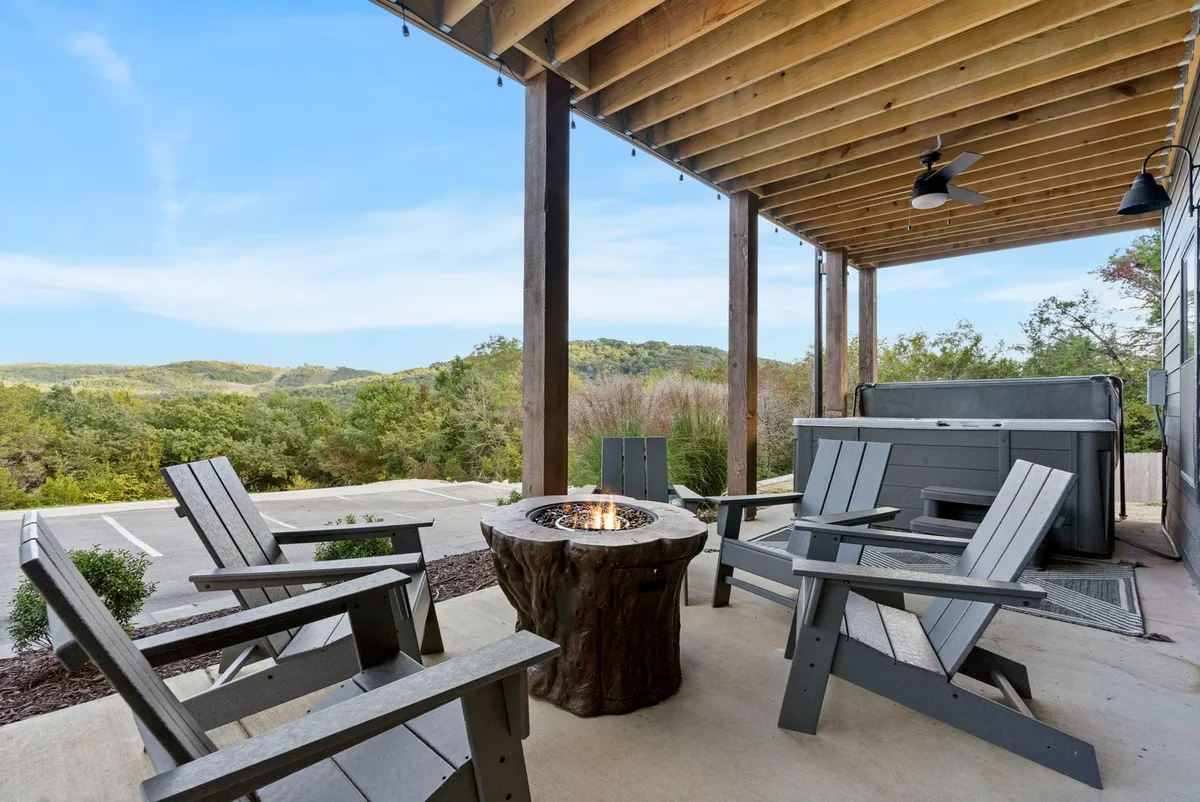 This exterior image captures a cozy fire pit surrounded by Adirondack chairs and a nearby hot tub, all set against a picturesque landscape view. The scene evokes relaxation, warmth, and the beauty of evenings spent outdoors in cooler months.