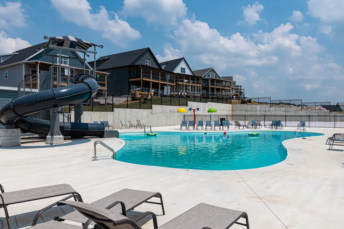 A vibrant exterior shot capturing a sparkling swimming pool surrounded by colorful umbrellas, lounge chairs, and a curving water slide. The scene overflows with joyful energy as families gather around the pool, suggesting an atmosphere of fun-filled summer days.