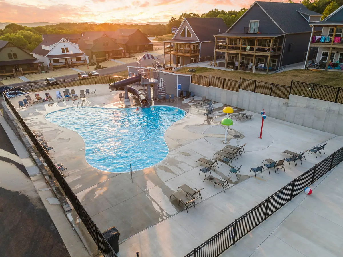 A vibrant outdoor pool scene featuring a swimming pool, an exciting water slide, colorful umbrellas, and lounge chairs. Children and families appear to be joyfully playing and relaxing under the sun.