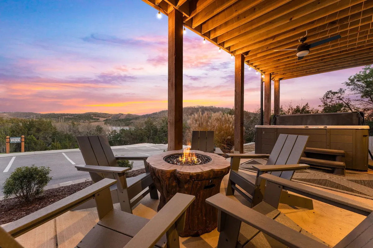 An inviting exterior scene with a fire pit surrounded by Adirondack chairs, a hot tub positioned to take in the sunset, and tranquil views of the surrounding landscape. The space is designed for intimate gatherings and relaxation under the open sky.