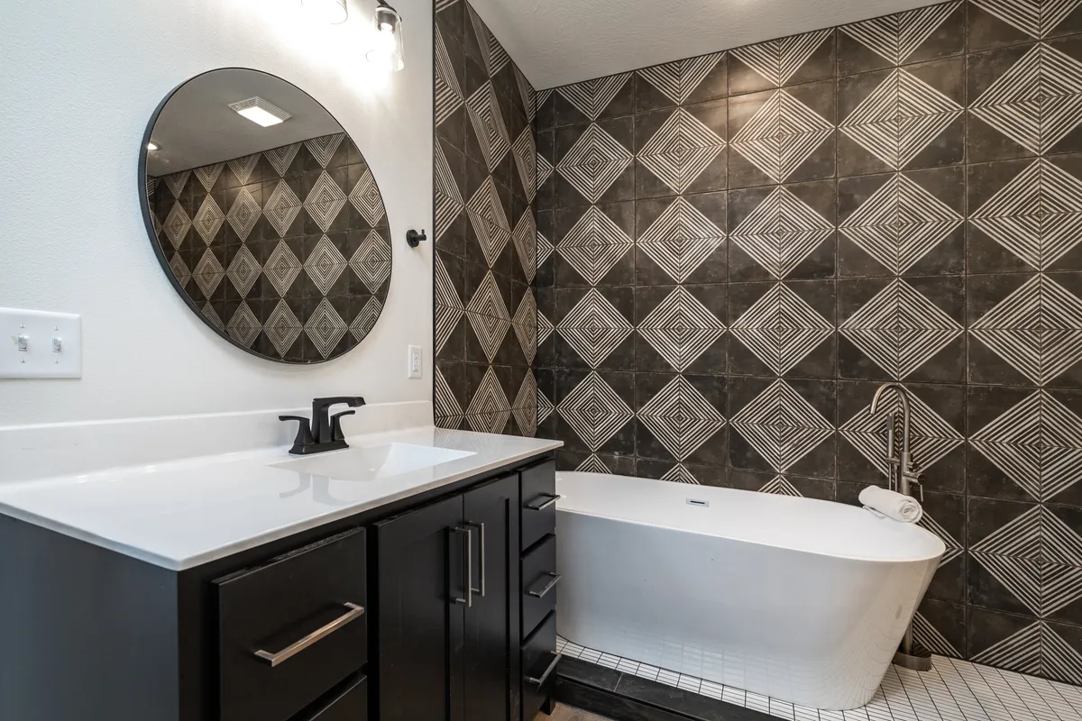 A spa-inspired ensuite bathroom featuring a freestanding bathtub against a geometric tile wall, a circular mirror, and a modern vanity. The space feels calming, sophisticated, and perfect for an indulgent self-care experience.