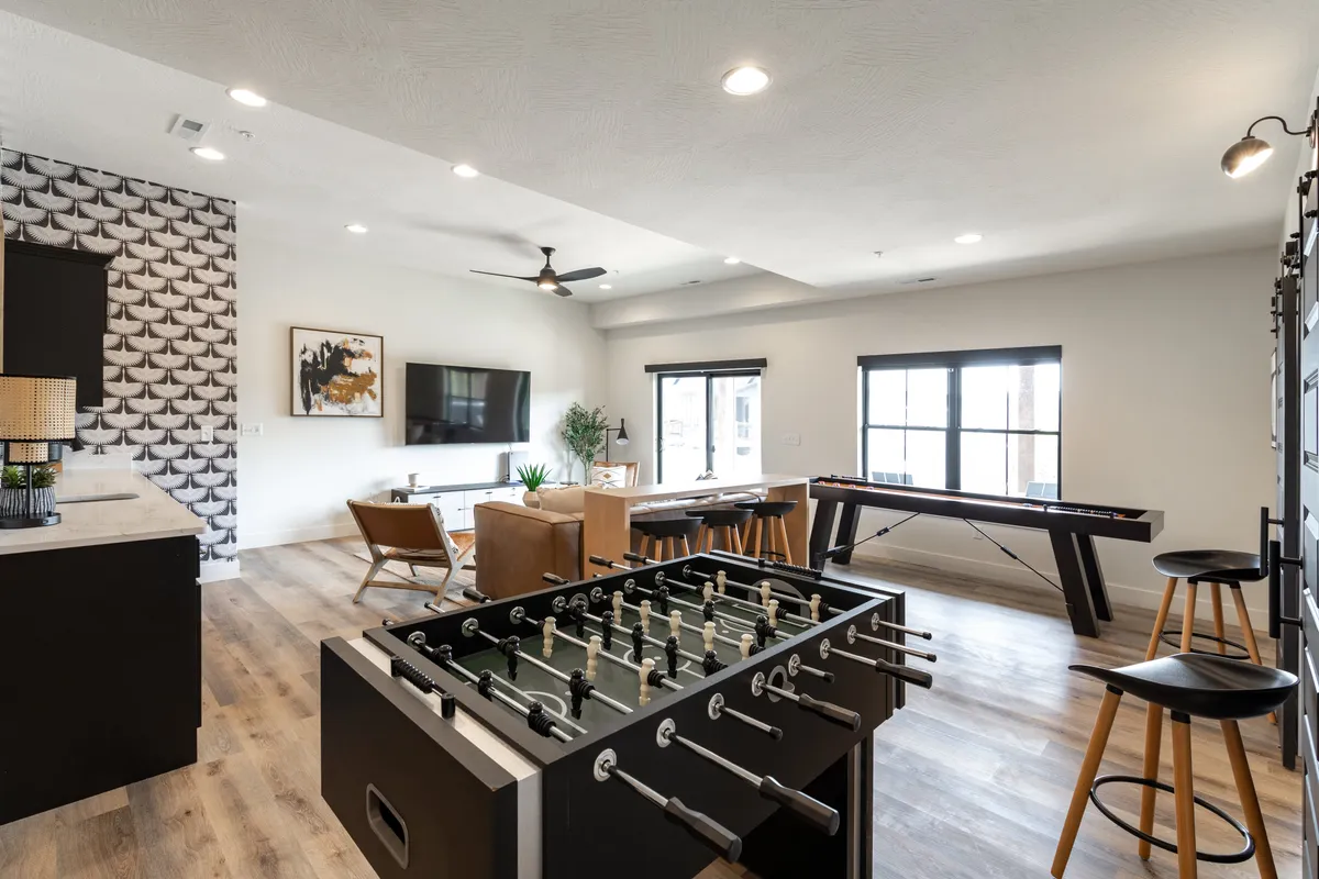 This interior image shows a lively game room featuring a foosball table, a cozy sofa seating area, a dining table, and a television. The space is designed for friendly competitions, casual gatherings, and relaxed movie nights.