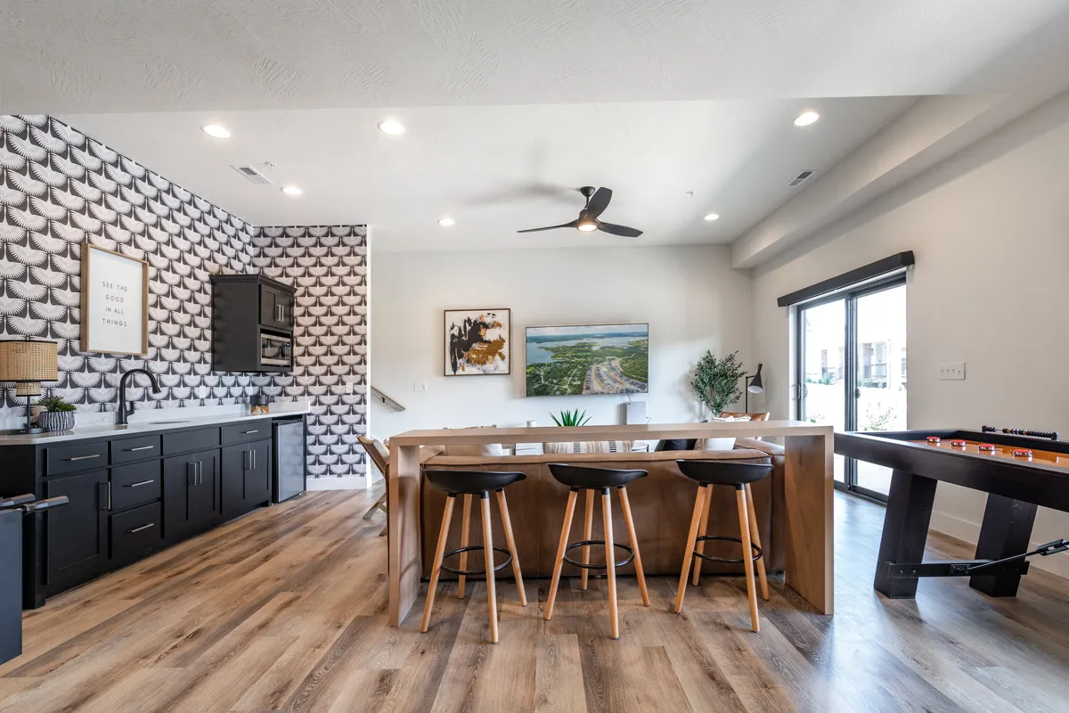 This bright interior shot highlights a space with black cabinetry, unique wallpaper, bar seating, artwork on the wall, and a foosball table. The wet bar/coffee bar area is seamlessly integrated with the gaming space, offering a hub for refreshments and socializing.