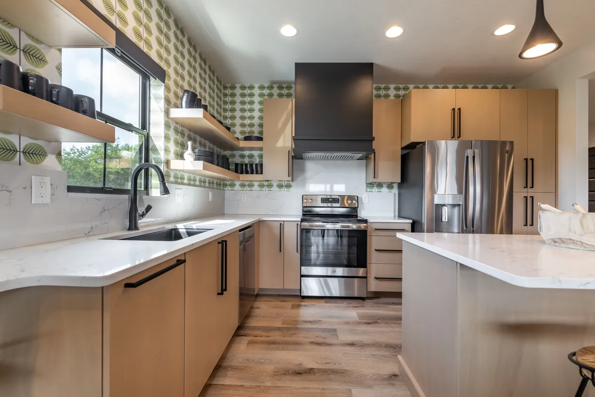 The image showcases a welcoming kitchen with a prominent island, stainless steel appliances, and a decorative wall adorned with green patterns. The open-concept design allows for plenty of space to cook and gather, with bar seating at the island inviting guests to join in the culinary action.